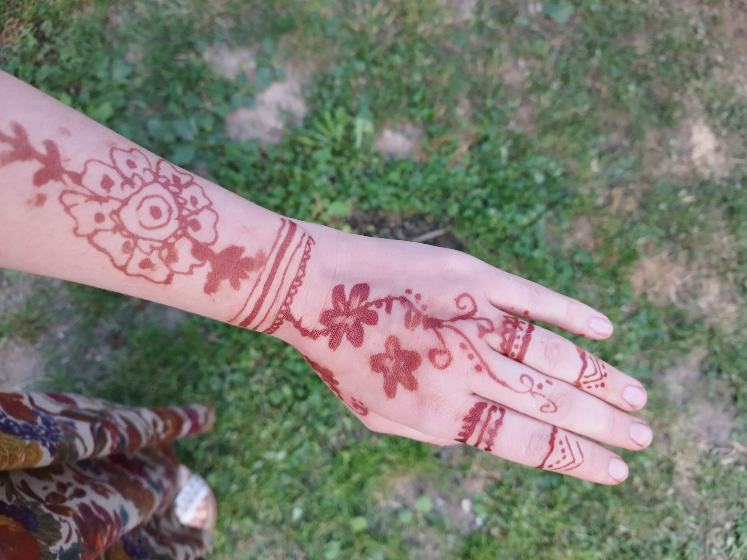 Női kar és kéz henna mintákkal, zöld fűben.