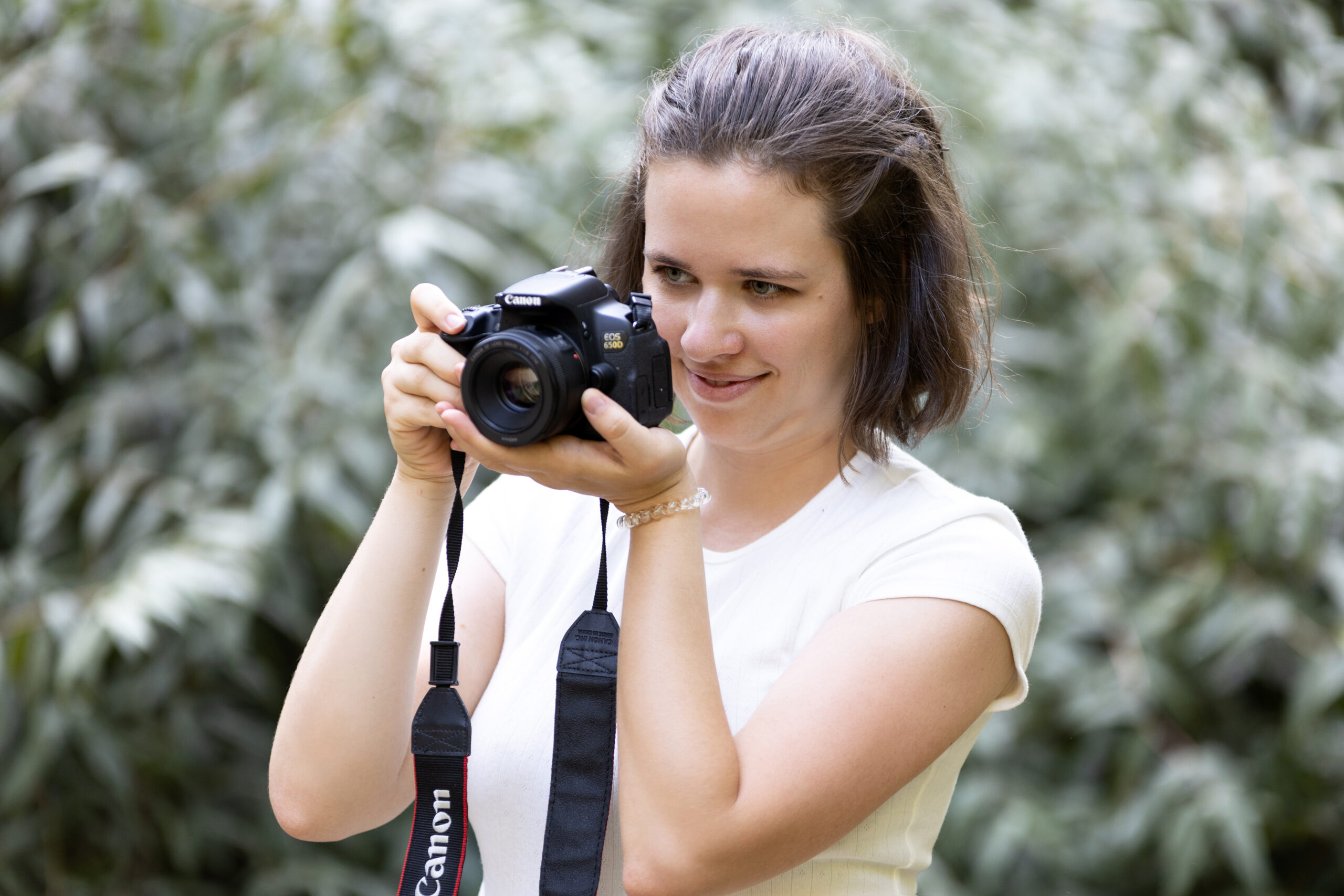 Nő Canon fényképezőgéppel fotóz mosolyogva a természetben.
